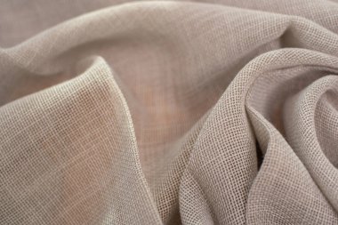 Açık bej kumaşı yarı şeffaf, dokuma dokusuyla kapatın. Kumaş yumuşak kıvrımlarla örtülmüş doğal dokusunu ve narin görünümünü vurguluyor..