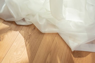 Beyaz şeffaf kumaş, arka planda hafif ahşap ve güneş ışınları. Saf hafif perde kumaşı.