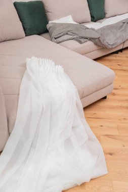 Beyaz tül bej bir kanepede yatıyor. Kanepede şeffaf kumaştan yapılmış bir perde..