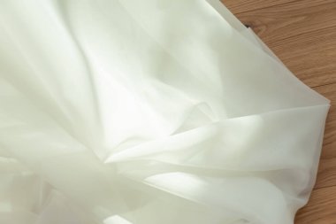 Beyaz şeffaf kumaş, arka planda hafif ahşap ve güneş ışınları. Saf hafif perde kumaşı.