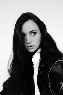 beautiful young woman with long hair in black leather jacket and white shirt on a light background