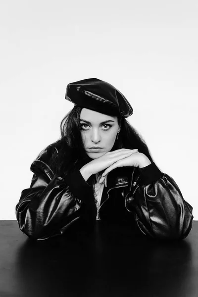 beautiful young woman in black leather jacket and hat posing on white background