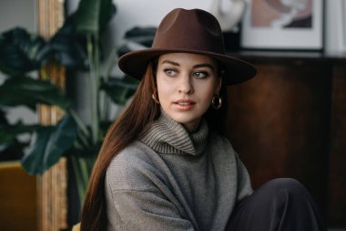 young pretty woman standing in studio with hat and looking away
