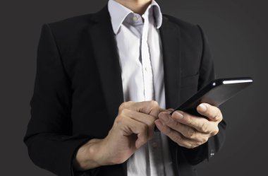 Siyah takım elbiseli bir işadamı iş verilerini görmek ve işi kontrol etmek için elinde cep telefonu tutuyor.