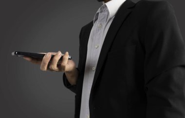 Siyah takım elbiseli bir işadamı iş verilerini görmek ve işi kontrol etmek için elinde cep telefonu tutuyor.