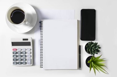 Ortasında boşluk olan boş beyaz bir defter. Beyaz masada bir hesap makinesi, bir cep telefonu ve bir kahve fincanı var, maket için. Metin ve grafik çalışmaları için boş alan.