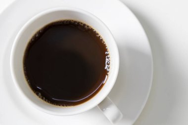 Beyaz fincan ve sade kahve, beyaz masanın üstünde.