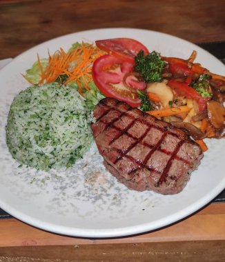 Sebzeli ızgara picanha bifteği, salata ve pirinç ahşap masada..