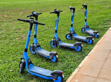 Görüntü, şehir ortamında kaldırımda bir dizi mavi elektrikli scooter gösteriyor. Muhtemelen çevre dostu şehir ulaşımını desteklemek için kullanılan bir kiralama şirketinden.