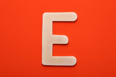 Alphabet letter E - White wood piece on orange foamy background