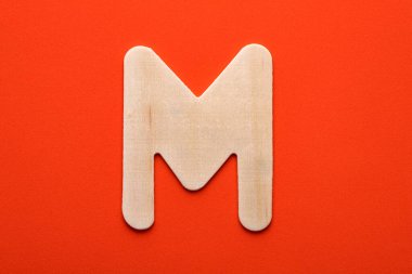 Alphabet letter M - White wood piece on orange foamy background