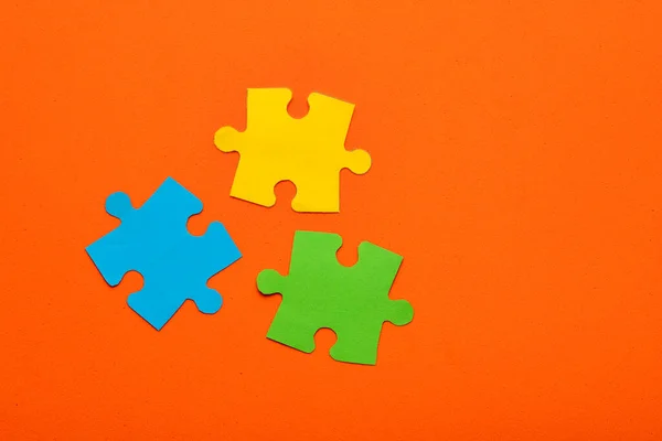 Three jigsaw puzzle pieces colored blue, green and yellow on orange background - Teamwork concept