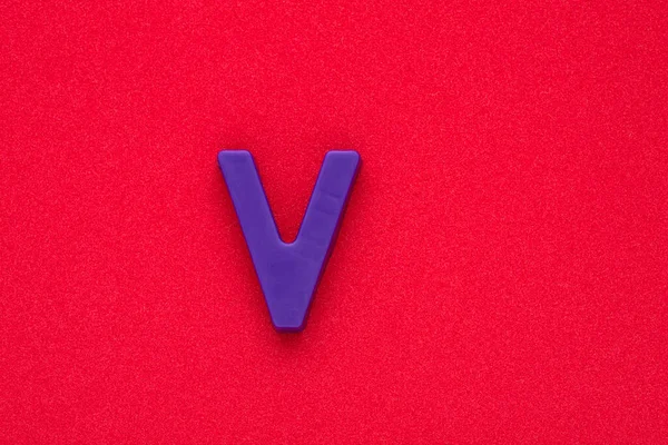 stock image Alphabet letter V - Violet colored plastic piece on red 032 c foamy background