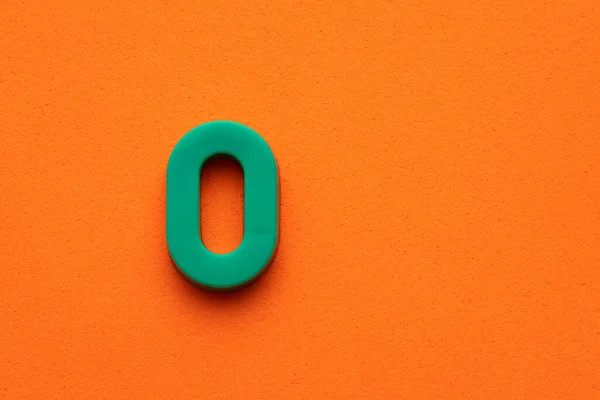 Letter O green plastic uppercase on orange foamy background