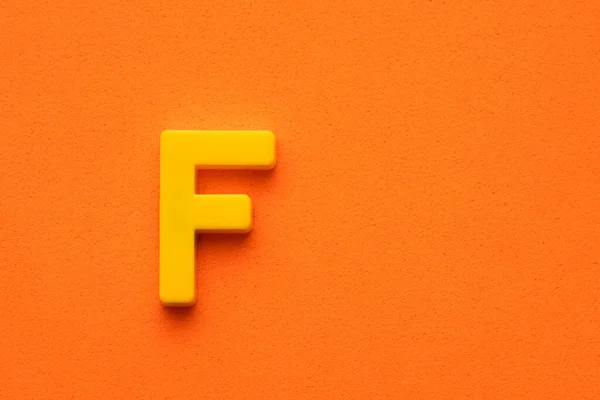Gelber Kunststoff Buchstabe Großbuchstabe Auf Orange Schaumigen Hintergrund — Stockfoto