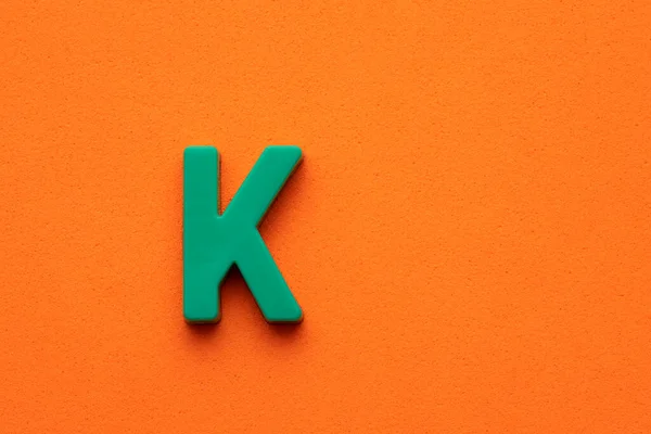 Letter K green plastic uppercase on orange foamy background