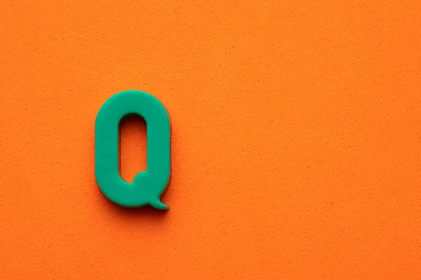 Letter Q green plastic uppercase on orange foamy background