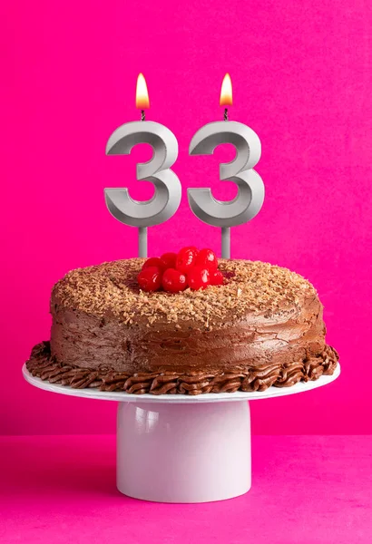Number 33 candle - Chocolate cake on pink background