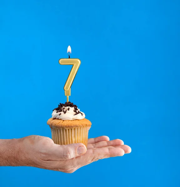 Hand delivering birthday cupcake - Candle number 7 on blue background