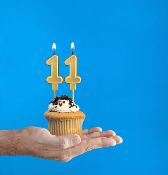 Hand delivering birthday cupcake - Candle number 11 on blue background