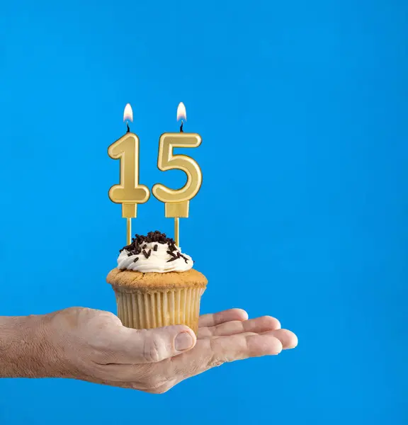 Hand delivering birthday cupcake - Candle number 15 on blue background