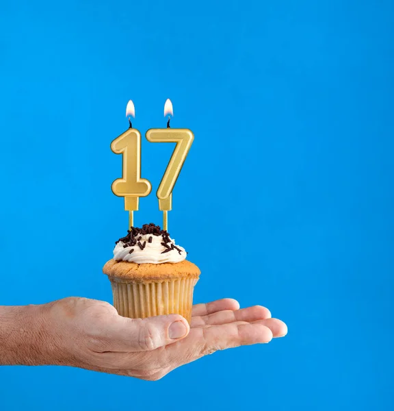 Hand delivering birthday cupcake - Candle number 17 on blue background