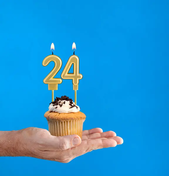 Hand holding a cupcake with the number 24 candle - Birthday on blue background