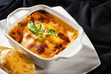 Beyaz kare tabakta taze fesleğen yapraklı İtalyan lazanyası.