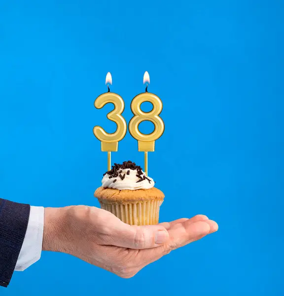 Hand delivering birthday cupcake - Candle number 38 on blue background