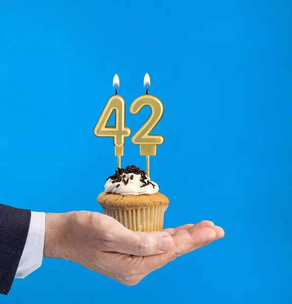Hand delivering birthday cupcake - Candle number 42 on blue background