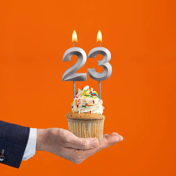 The hand that delivers cupcake with the number 23 candle - Birthday on orange background