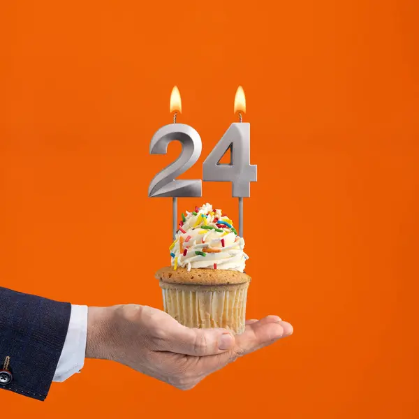 Hand holding birthday cupcake with number 24 candle - background orange