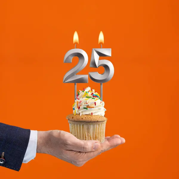 The hand that delivers cupcake with the number 25 candle - Birthday on orange background
