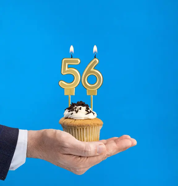 Hand delivering birthday cupcake - Candle number 56 on blue background
