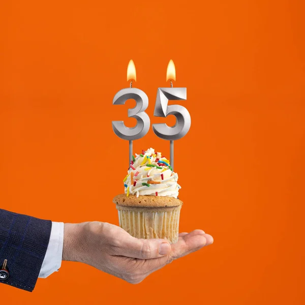 The hand that delivers cupcake with the number 35 candle - Birthday on orange background