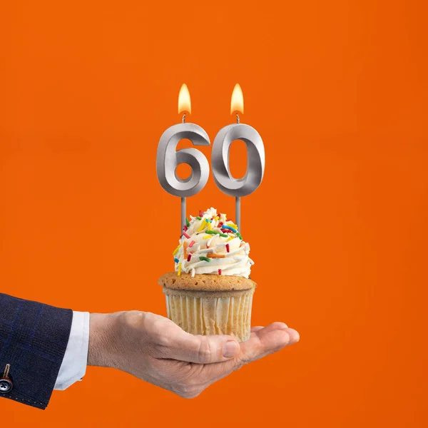 The hand that delivers cupcake with the number 60 candle - Birthday on orange background