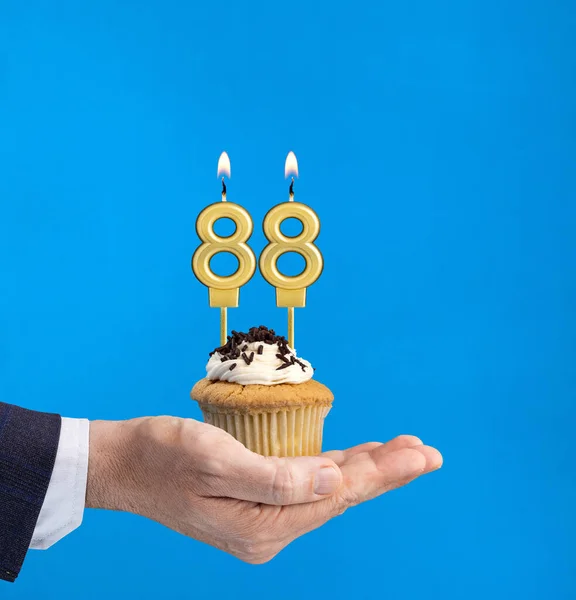 手拿着一个印有88号蜡烛生日蓝色背景的纸杯蛋糕 — 图库照片