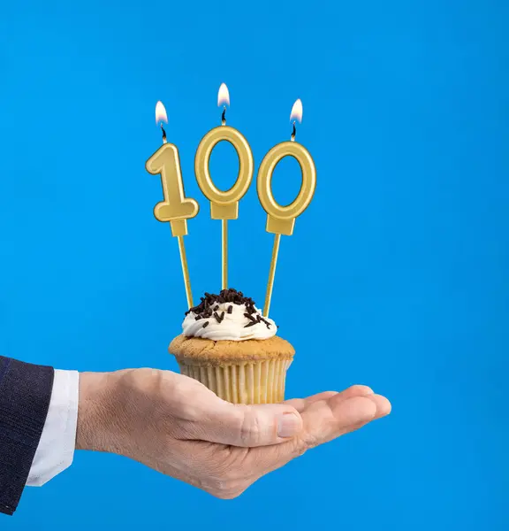 Hand delivering birthday cupcake - Candle number 100 on blue background