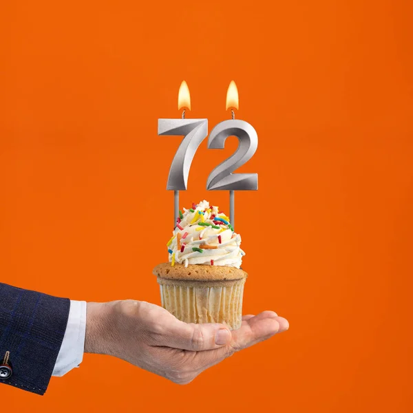 The hand that delivers cupcake with the number 72 candle - Birthday on orange background