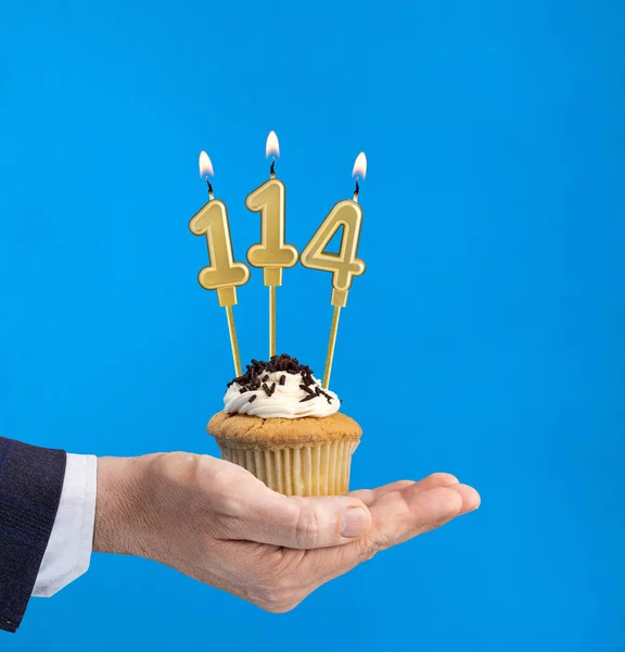 Hand delivering birthday cupcake - Candle number 114 on blue background
