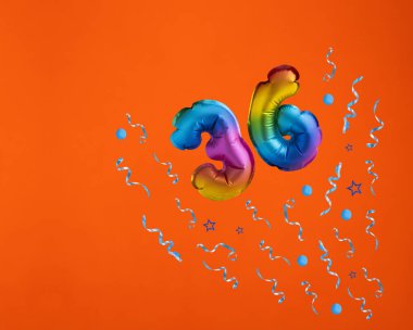 36 numaralı çoklu renkli balon turuncu arka planda konfeti patlaması. Doğum günü kartı