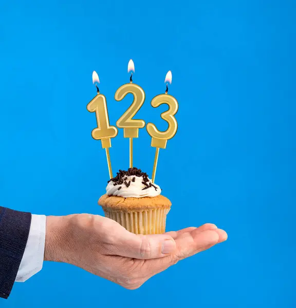 Hand holding a cupcake with the number 123 candle - Birthday on blue background