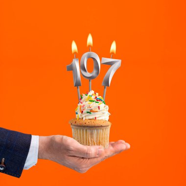 Hand holding birthday cupcake with number 107 candle - background orange clipart