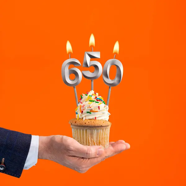 stock image The hand that delivers cupcake with the number 650 candle - Birthday on orange background