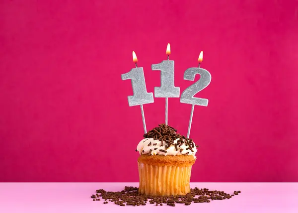 stock image Birthday celebration with candle number 112 - Chocolate cupcake on pink background