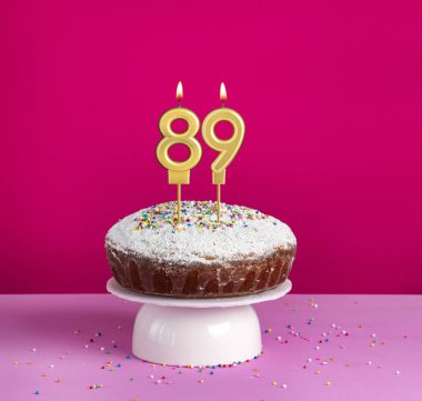 Pembe arka planda 89 numaralı mumlu doğum günü pastası.