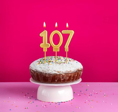 Birthday cake with number 107 candle on pink background clipart