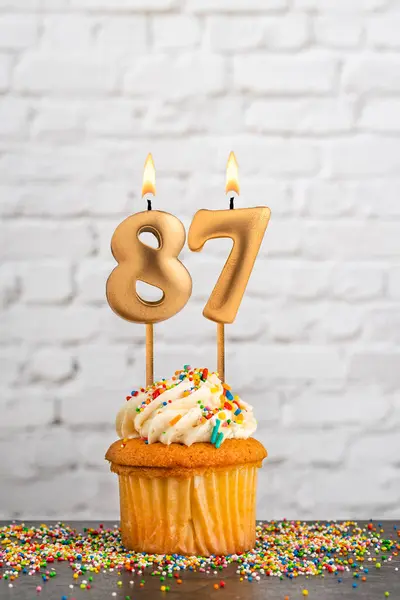 stock image Golden birthday candle number 87 with cupcake - White block wall background