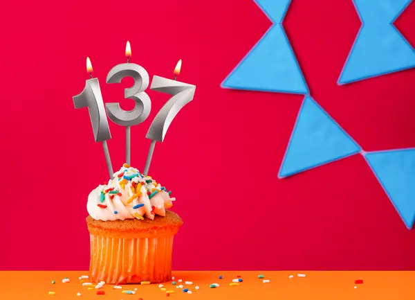 stock image Number 137 candle with birthday cupcake on a red background with blue pennants