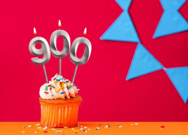 Kırmızı arka planda mavi flama ve doğum günü pastası olan 900 numaralı mum.